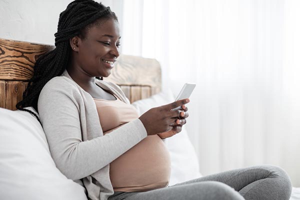 African American pregnant woman smiling as she looks at Lifetime's Adoption Option app on her phone